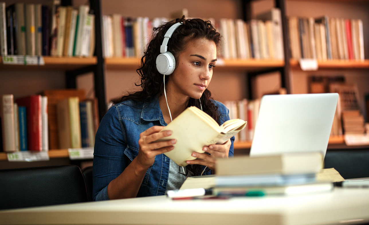 En student sitter i biblioteket med en dator och studerar. Foto.