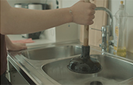 En hand som håller en vaskrensare över diskhon i ett kök. 
