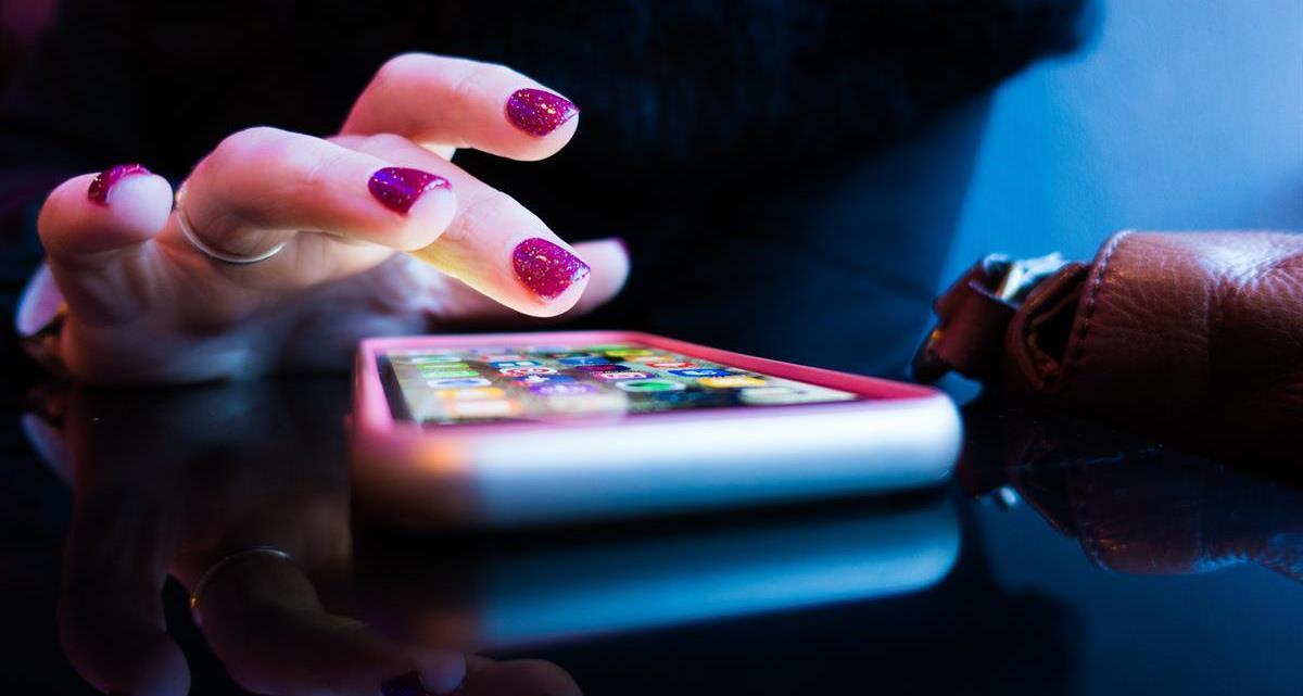 Foto som visar en hand med nagellack som pekar på en mobilskärm.