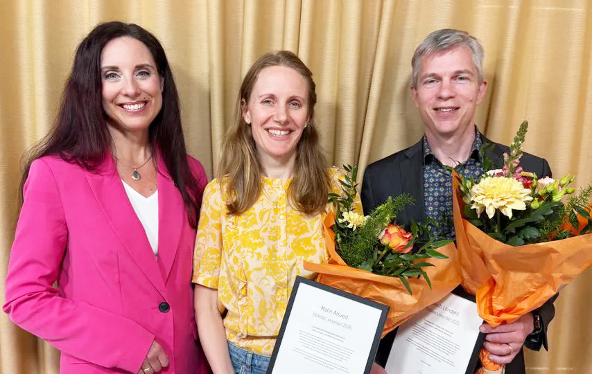 Photo of three people with flowers and diplomas.