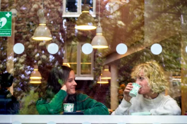 Två personer som sitter och dricker kaffe bakom en glasvägg.