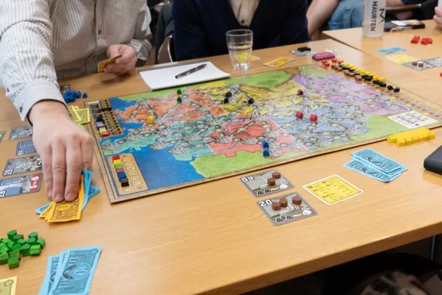 Ett bord med ett brädspel, händer på spelande personer syns. Foto.