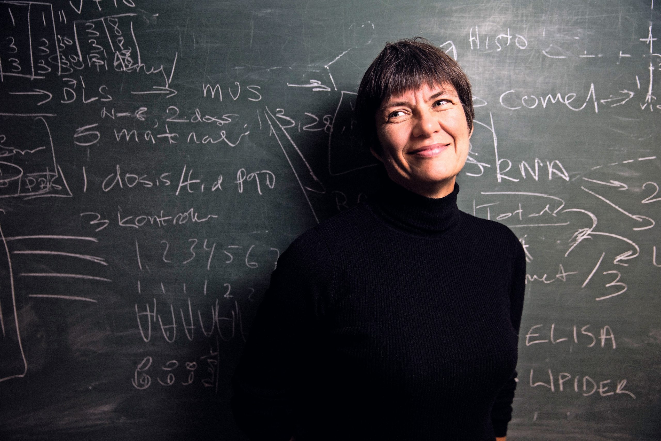 Photo of a woman in front of a blackboard with white writing on it.