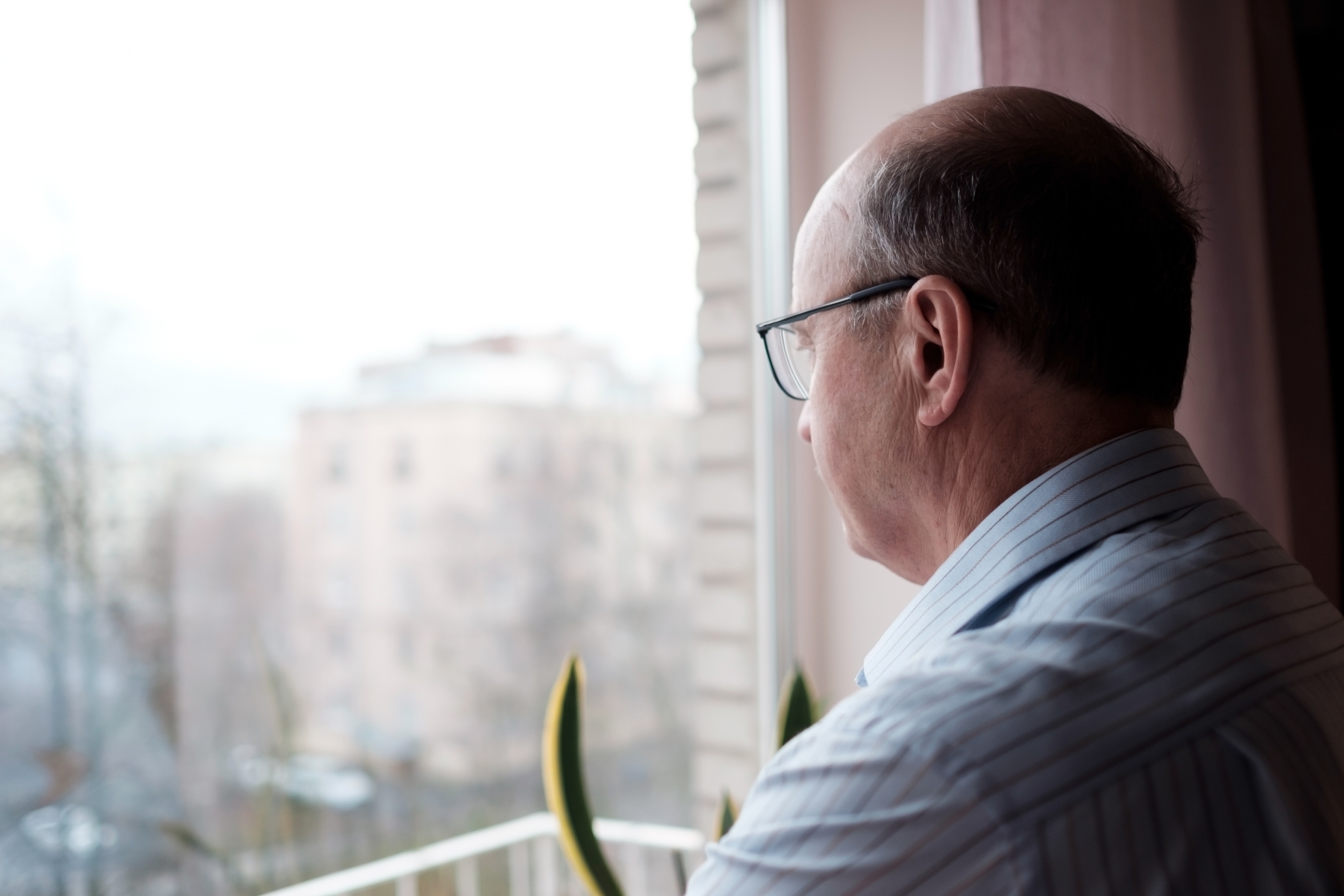 988 51753878 elderly caucasian man looking out window with lonely