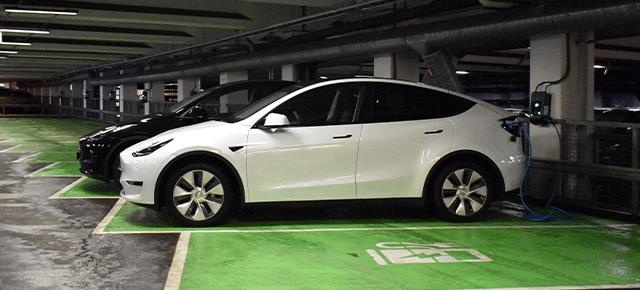 Två elbilar står parkerade på laddplatser i ett parkeringsgarage.