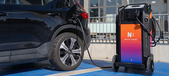 Flyttbar snabbladdare inkopplad i en bil på parkeringsplats.