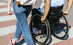 A man in a wheelchair and a woman crossing a street.