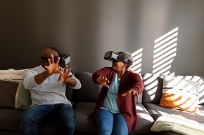 Man and woman sitting in a sofa wearing VR headsets.