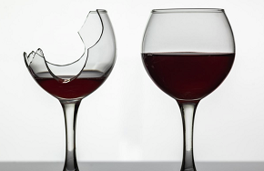 Två vinglas med rödvin i varav det ena glaset är söndrigt.