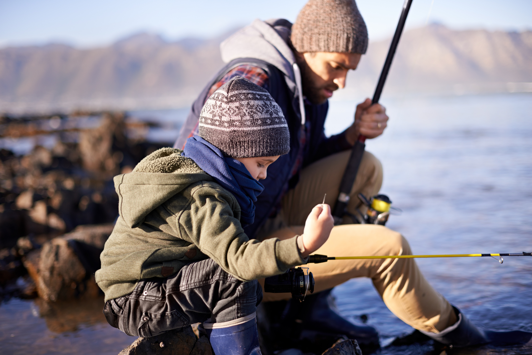 Pojke och pappa sitter nere vid en sjö med varsitt fiskespö i handen.