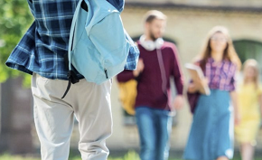 Unga studenter utomhus, rygg med en blå ryggsäck över axeln.