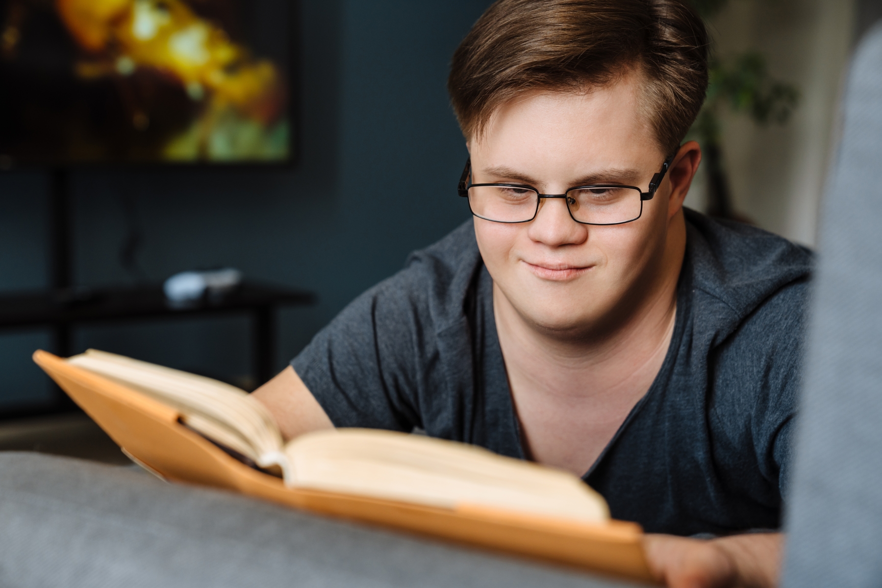 1230 49176444 young man with down syndrome reading book while lying on