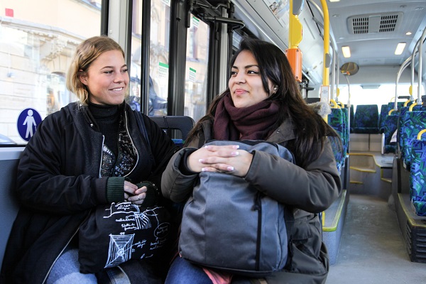 Two young, smiling women riding a bus.