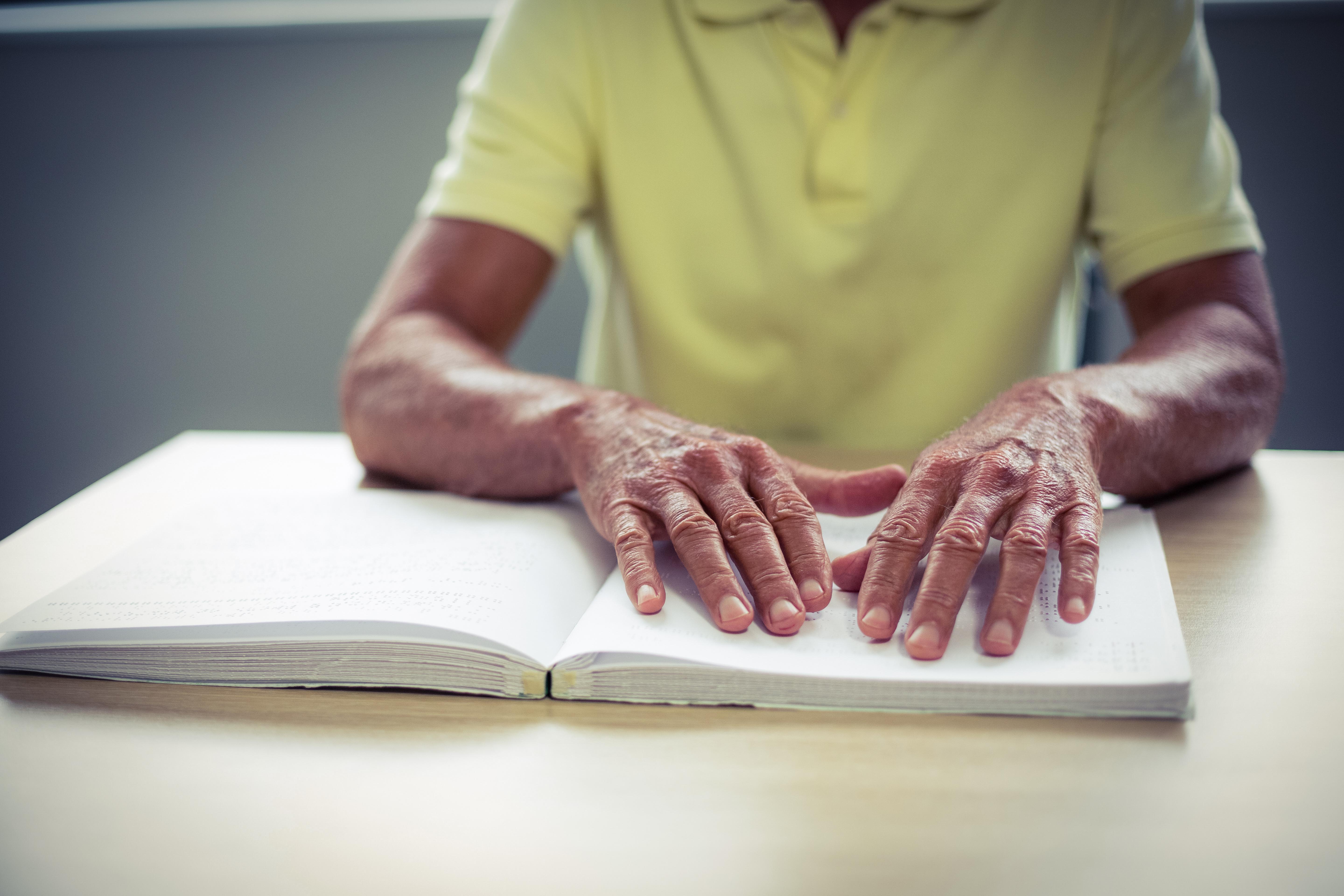 Bild på två äldre händer som läser en bok med braille. 