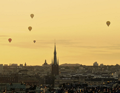 View of a city with yellow sky and hot air balloons.
