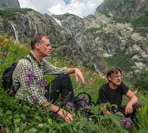 Två män sitter på en blommig sluttning i bergen