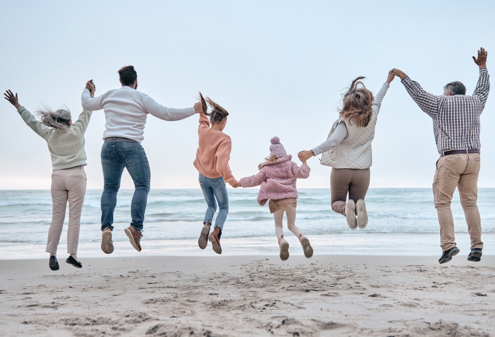 Six persons of three generations jumping in the air holding hands on a beach
