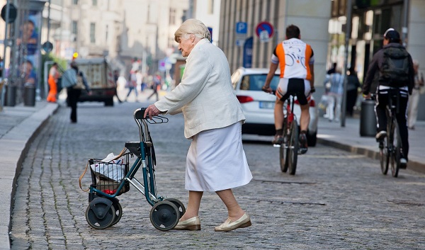 Äldre kvinna går med rollator öven vägen i stadsmiljö