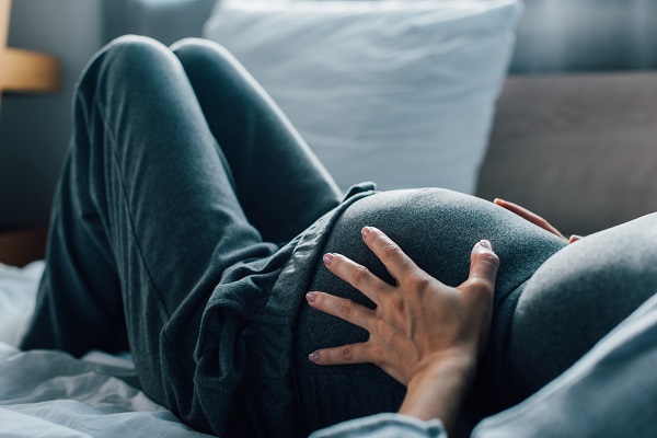 Gravid kvinna som ligger på sängen med händerna på magen, magen i fokus