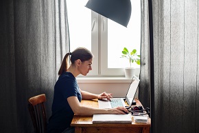 Kvinna sitter vid skrivbord framför laptop