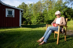 Äldre kvinna sitter utomhus i solen och tittar på en surfplatta