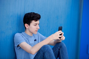 Tonåring sitter lutad mot en vägg och tittar på sin telefon