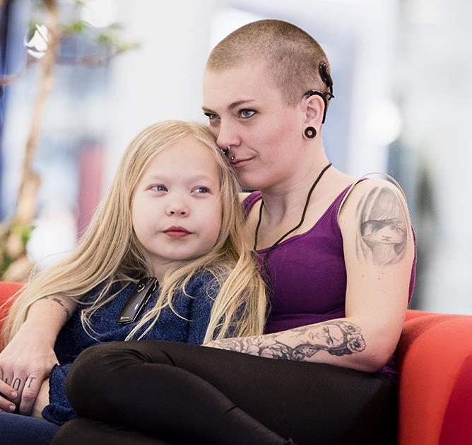Mamma med implantat sitter i soffa och kramar sin dotter.