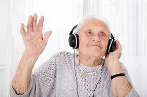 Leende äldre kvinna lyssnar på musik ur hörlurar.
