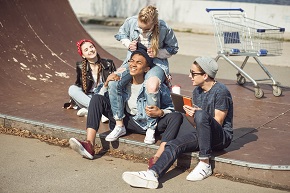 Fyra glada ungdomar sitter ute vid en skateramp.