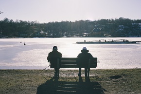 Två personer sitter på en parkbänk och tittar ut över vatten.