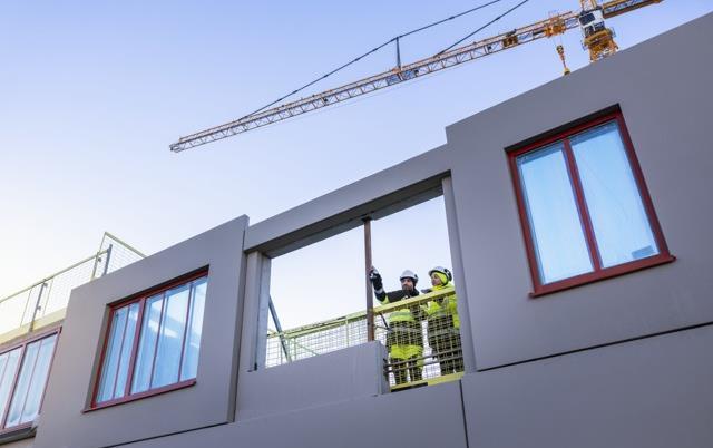 Två byggarbetare står och pekar uppe på ett bygge (bild från Scandinav)