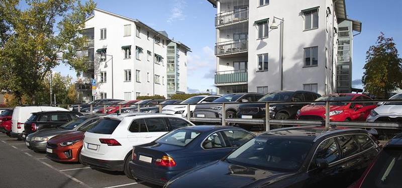 Bilparkering med många bilar parkerade, framför flerfamiljshus.