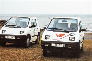 Två vita elbilar står parkerade vid havet.