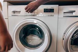 Fronten av en tvättmaskin som fyllts med vit tvätt samt en hand som vrider på vredet och sätter igång maskinen.