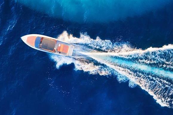 Motorbåt på blått hav med svallvågor efter, sedd rakt uppifrån.