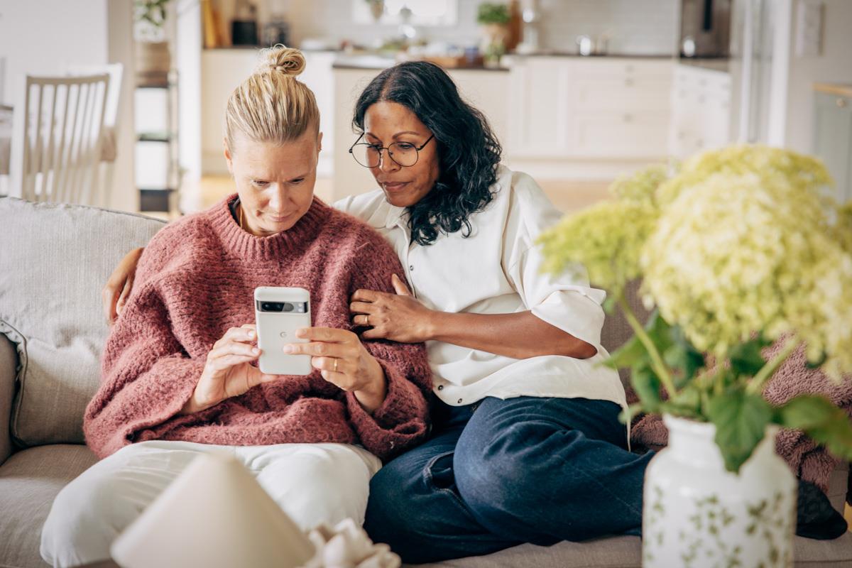 Två kvinnor sitter i soffa och tittar gemensamt i en mobil