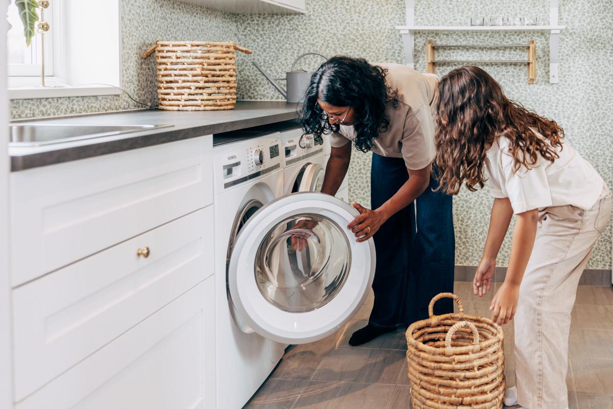 En kvinna och ett barn laddar en tvättmaskin.