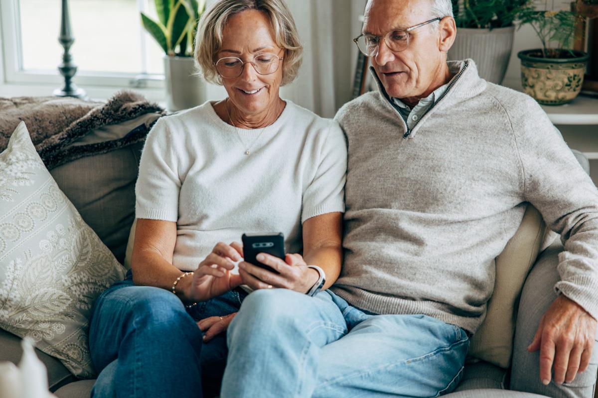 Ett äldre par sitter i en soffa och tittar i mobilen tillsammans.