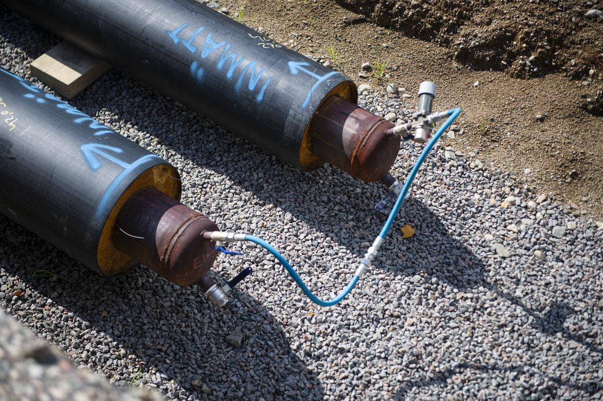 Ändar av två stycken fjärrkylarör som ligger på grus i en grop i solskenet.