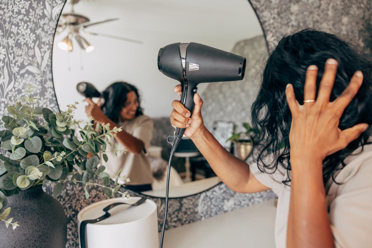 Kvinna torkar håret med en hårtork framför en rund spegel.