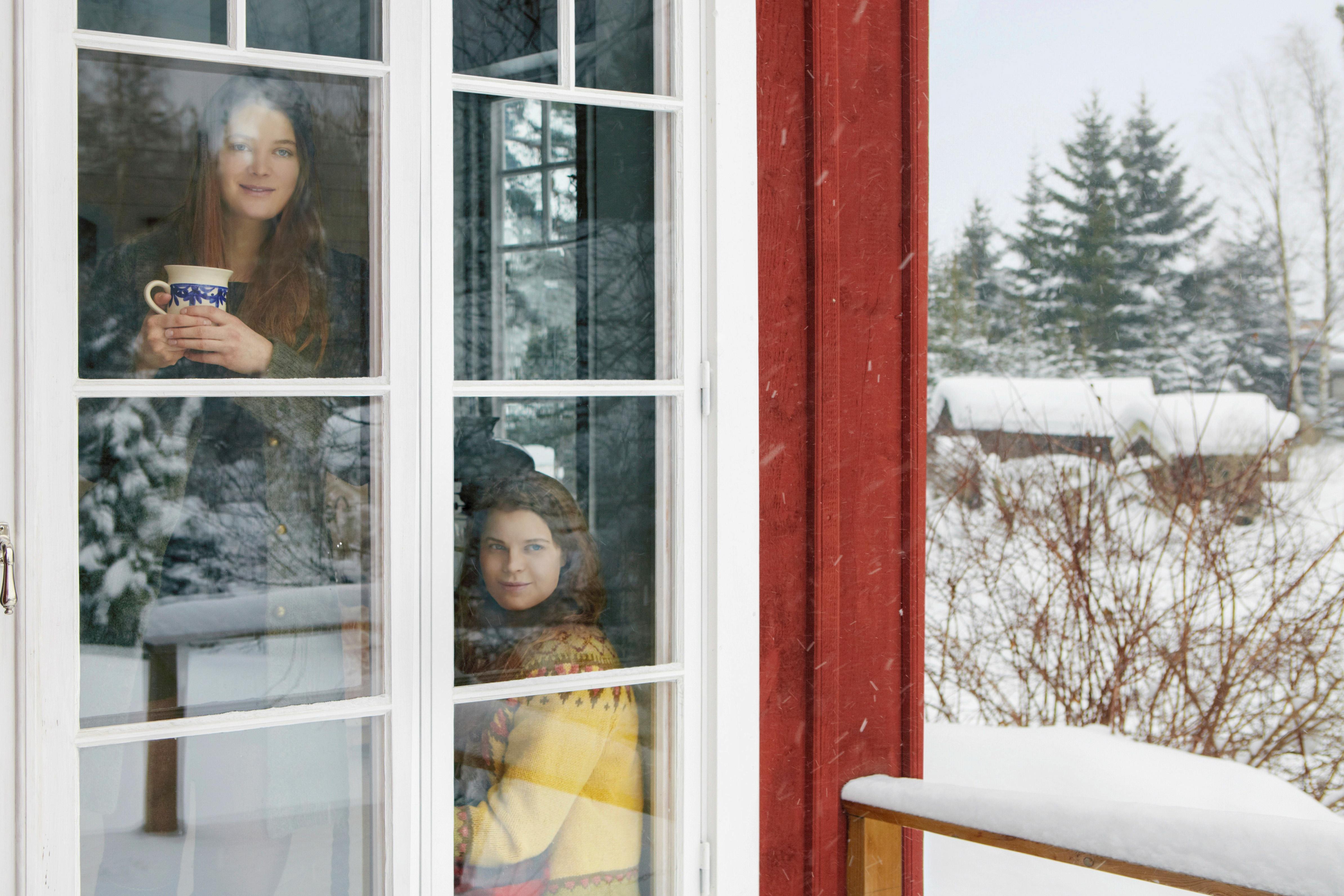 Två kvinnor ser ut genom ett fönster på ett vintrigt landskap.