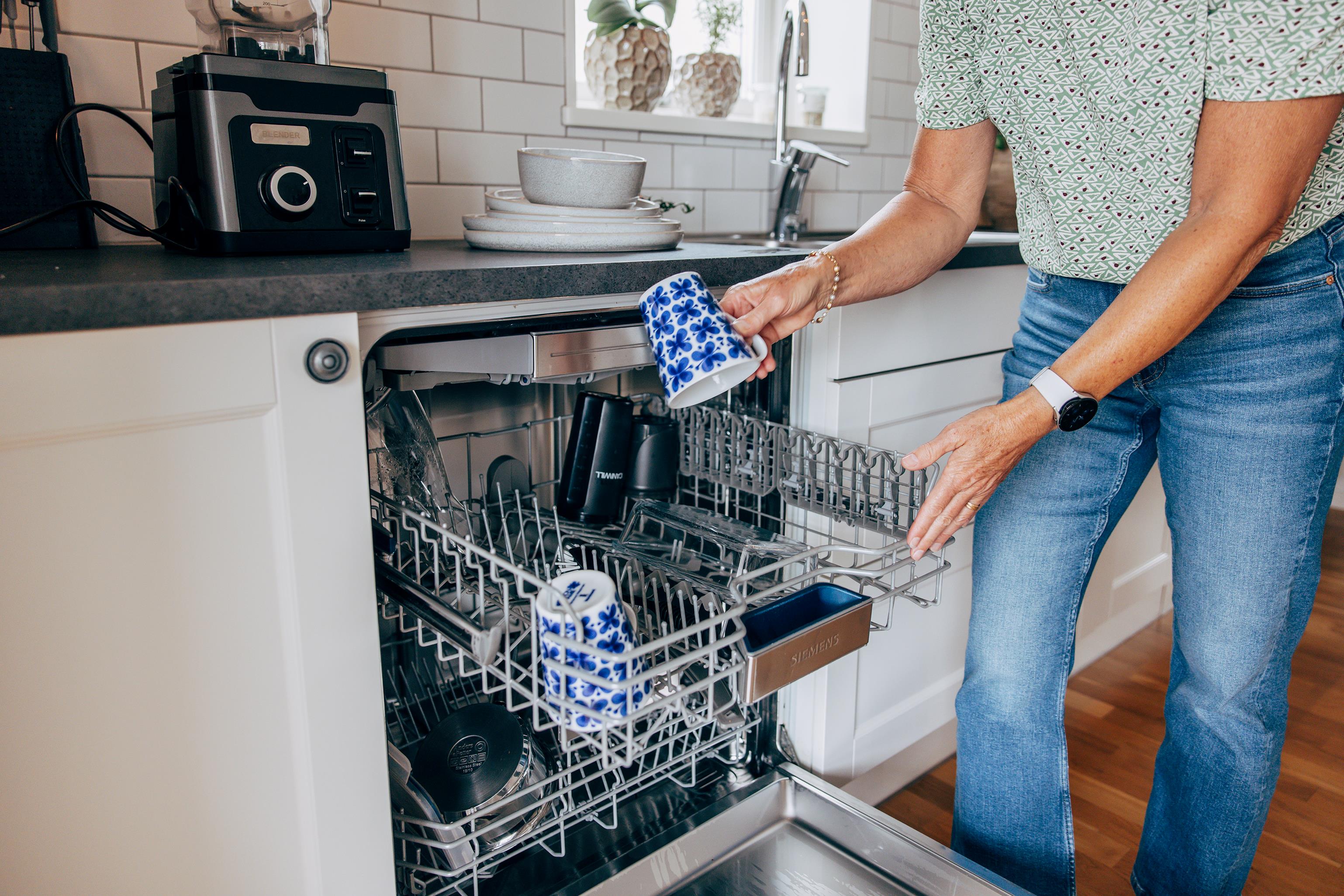 Kvinna ställer in blåmönstrade kaffekoppar i en öppen diskmaskin.