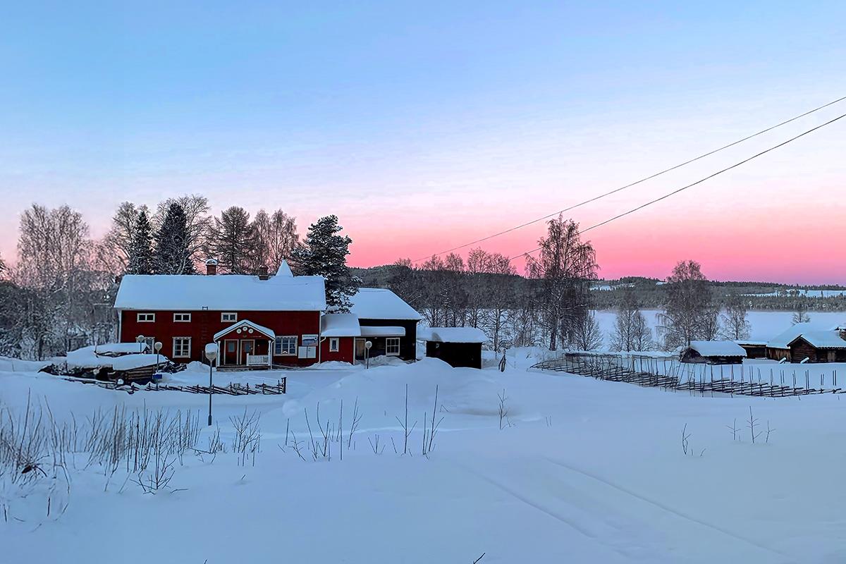 Rött hus i blå skymning i vinterlandskap.