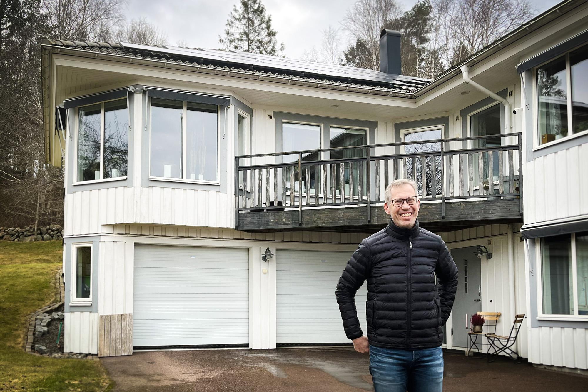 Glad man står framför ett vitt hus med solpaneler.