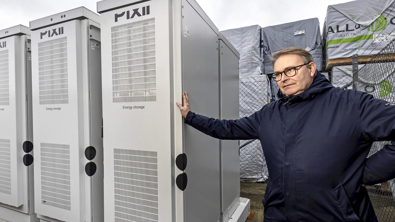 Man står och håller sin hand på ett av stora batterier i ett batterilager utomhus